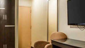 Una camera d'albergo con un letto, una scrivania, una sedia, una televisione e due armadi.