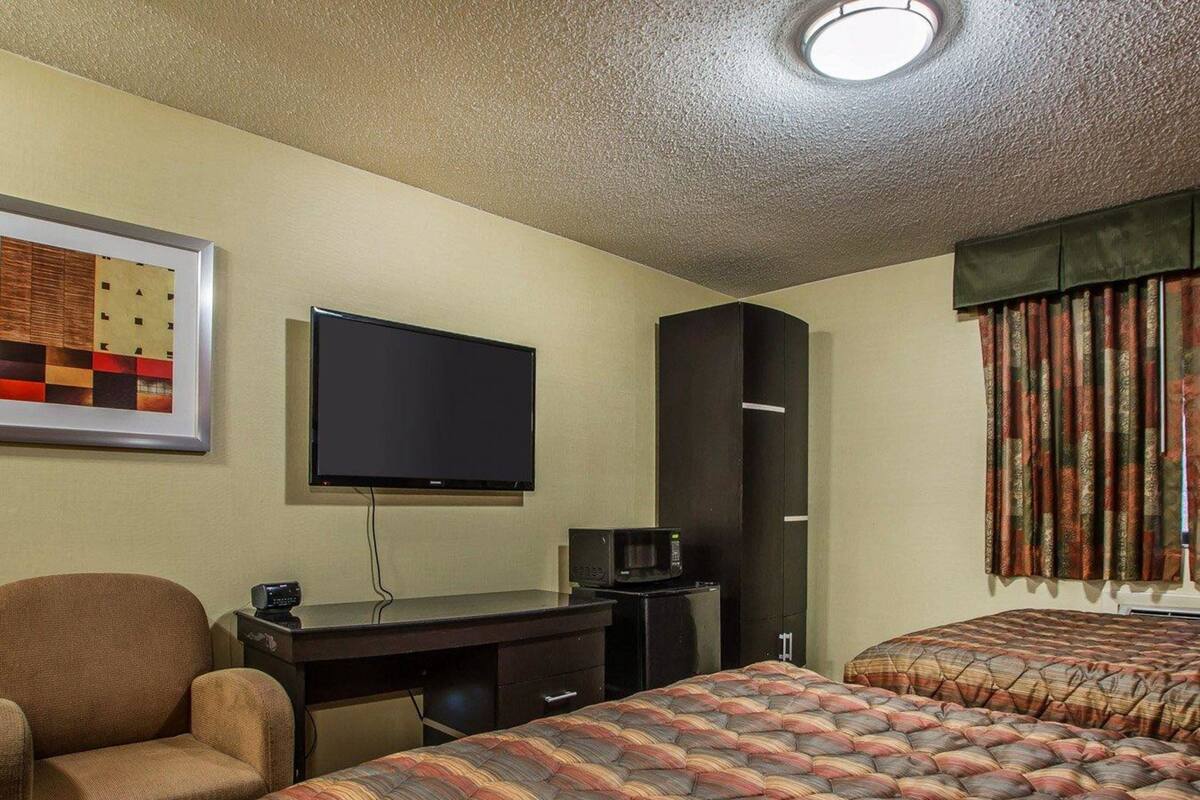 A hotel room with two beds, a desk with a flat-screen TV, a chair, and a wardrobe.