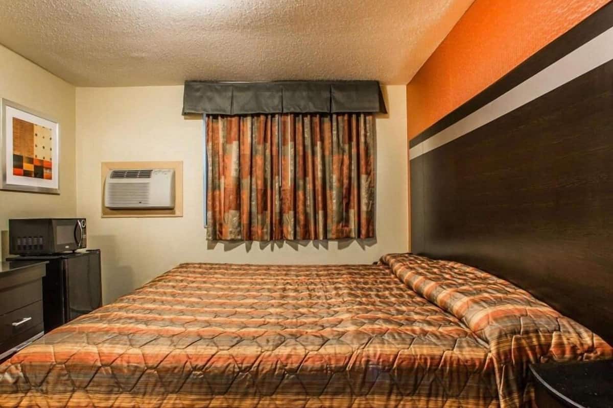 A hotel room with a bed, a desk with a computer, and a wall-mounted air conditioner.