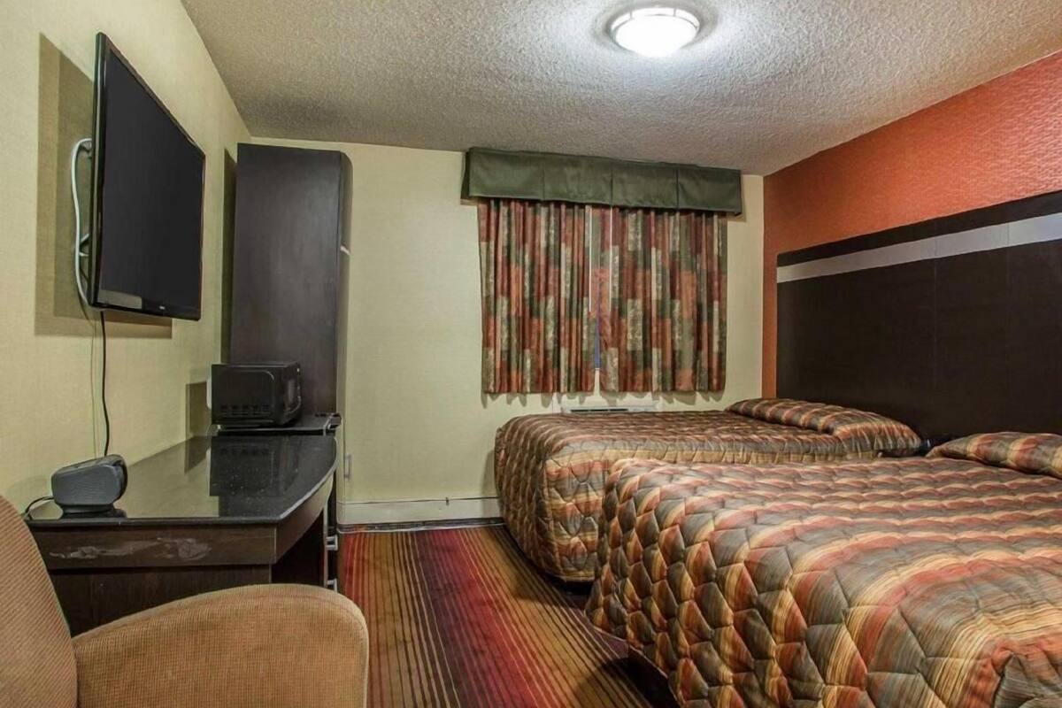 A hotel room with two beds, a desk with a television, and a chair.