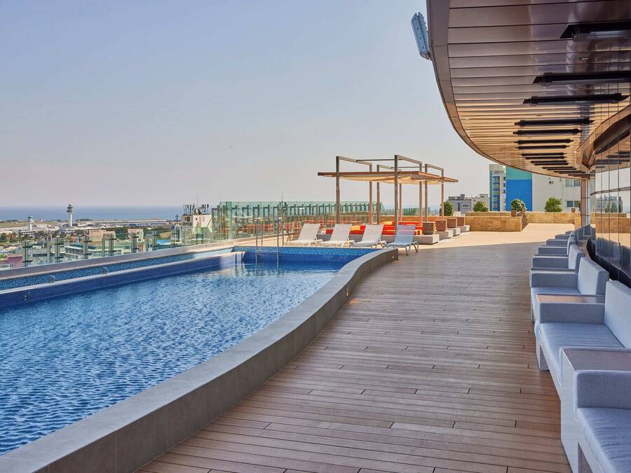 A rooftop pool with a view of the city skyline, lounge chairs, and a covered seating area.