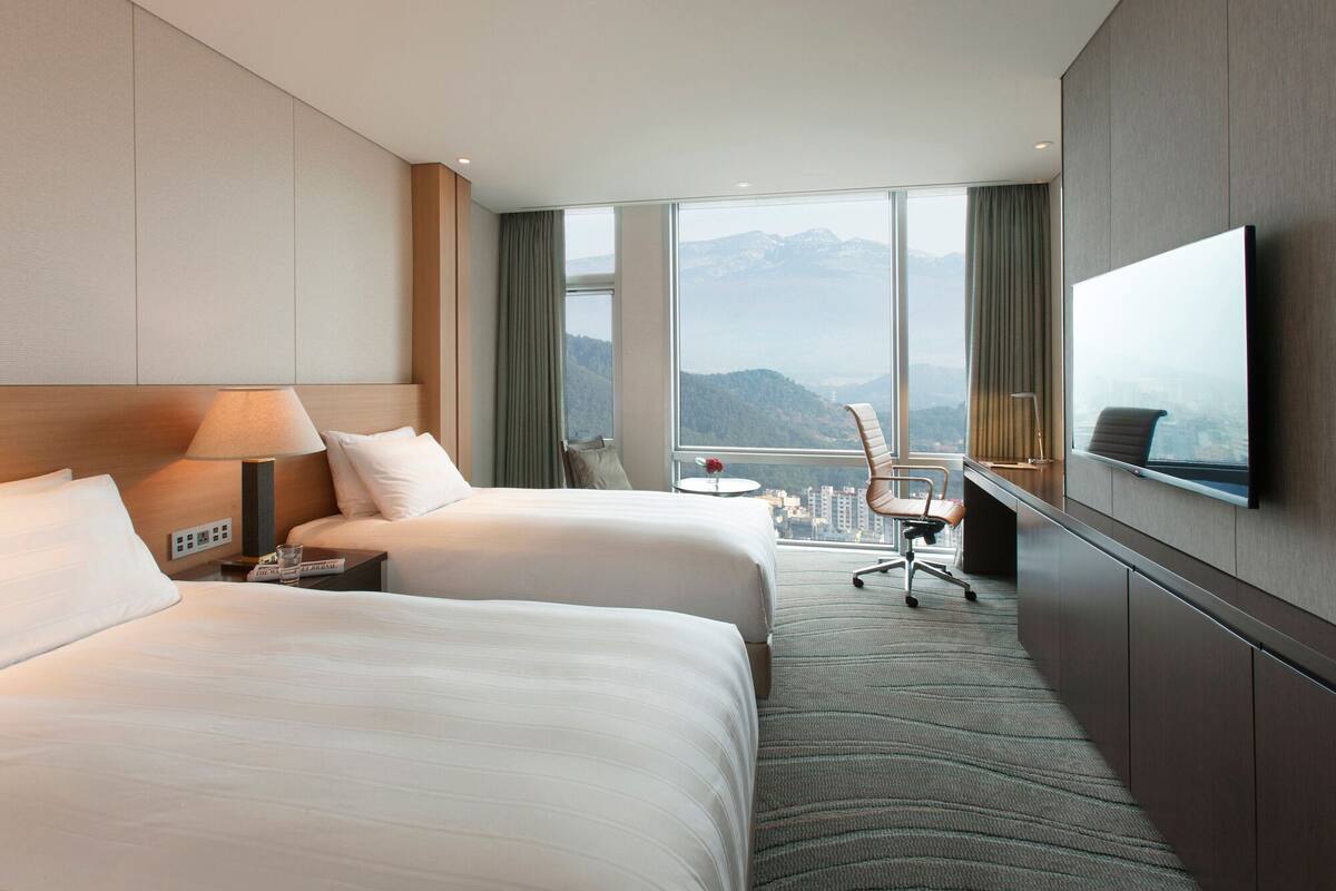 Habitación de hotel con dos camas, un escritorio, una silla, un televisor y vistas a las montañas.
