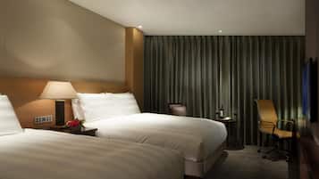 A hotel room with two beds, a desk with a lamp, a chair, a television, and a curtain.