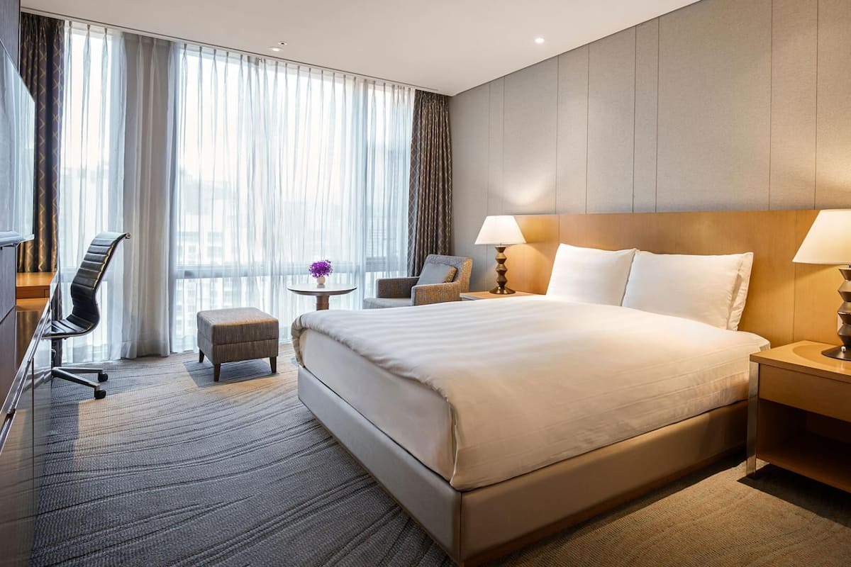 Une chambre dâhĂŽtel avec un grand lit, un bureau, une chaise, une tĂ©lĂ©vision et une fenĂȘtre avec des rideaux.