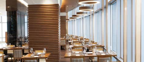 A modern restaurant with wooden slatted walls, long tables, and hanging pendant lights.
