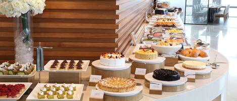 A buffet with various desserts and pastries, including cakes and tarts, arranged on a counter with a wooden backdrop.