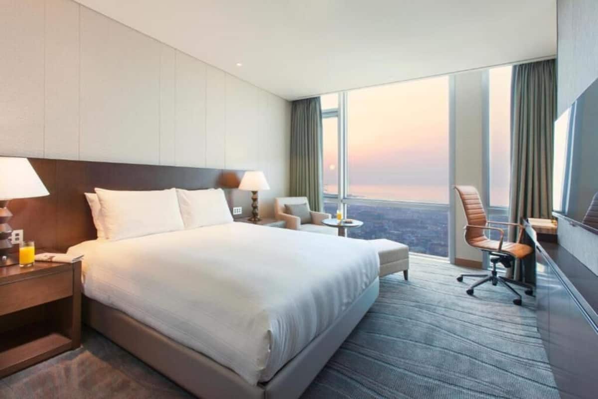 Une chambre dâhĂŽtel avec un grand lit, un bureau, une chaise et une vue sur le paysage urbain.