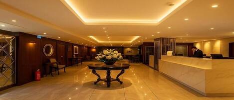 A hotel lobby with a reception desk, a round table with flowers, and a fire extinguisher.