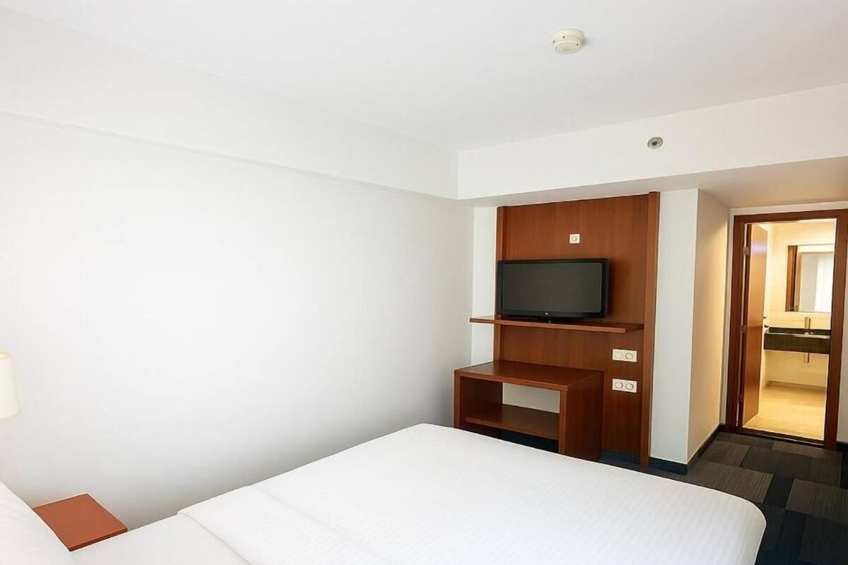 A hotel room with a large bed, a television on a wooden stand, and a door leading to a bathroom.