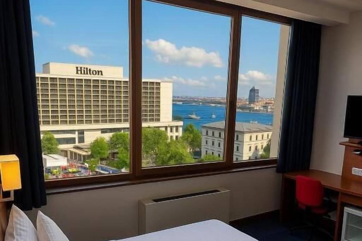 A hotel room with a large bed, a desk, and a view of the city and water.
