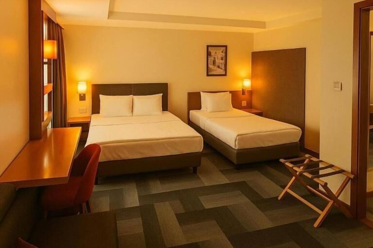 A hotel room with two beds, a desk, a chair, and a small table.