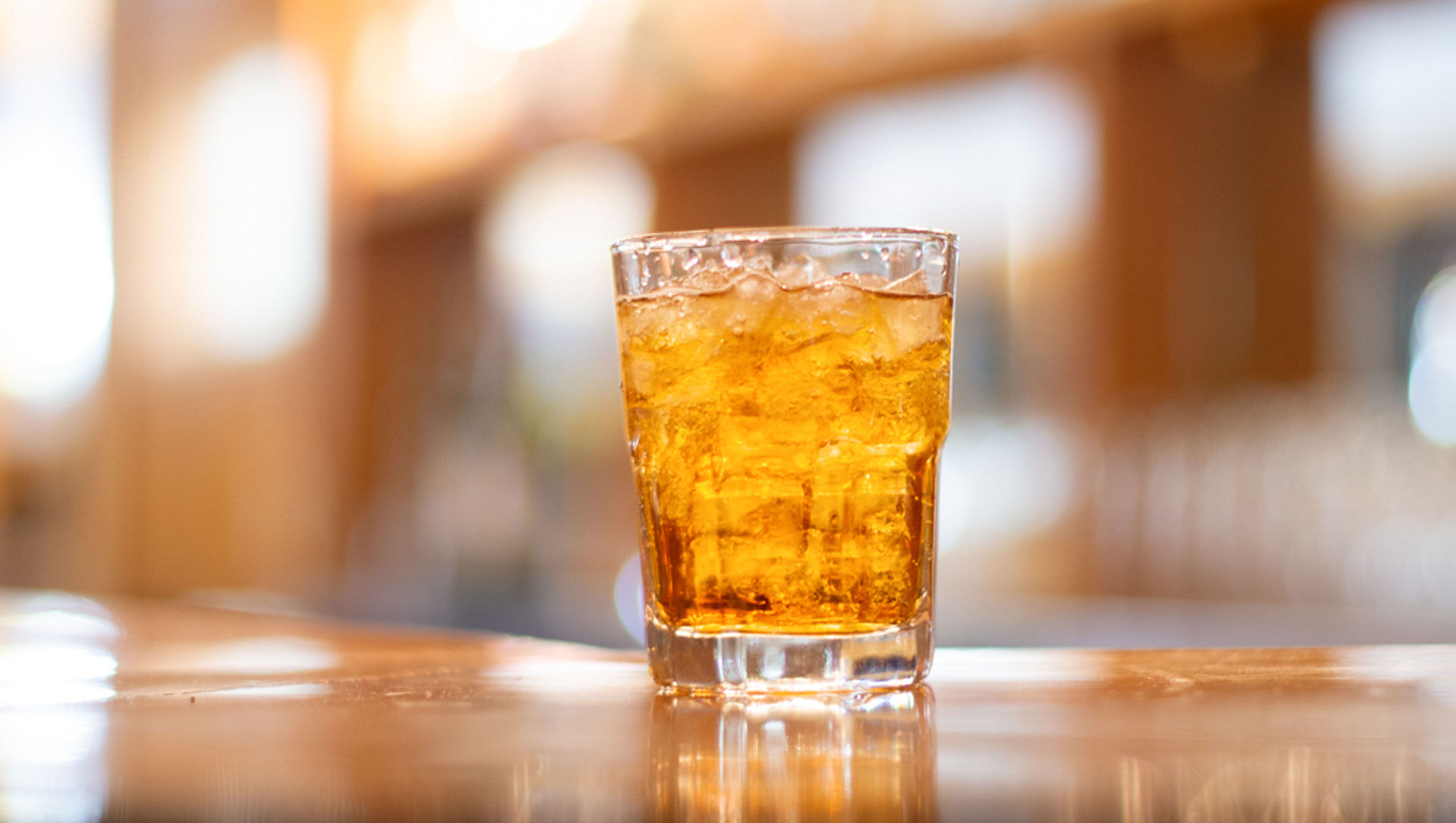 Un verre d’une boisson de couleur ambrée, posé sur une surface réfléchissante.