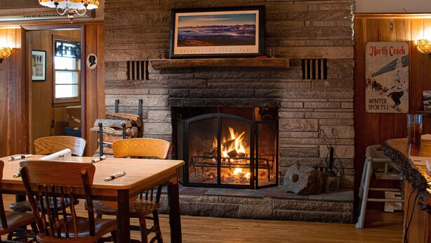 A cozy room with a fireplace, wooden furniture, and a framed picture of the Adirondack High Peaks.