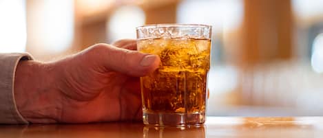En hånd holder et glas med en ravfarvet drik, muligvis te eller whisky, med isterninger.