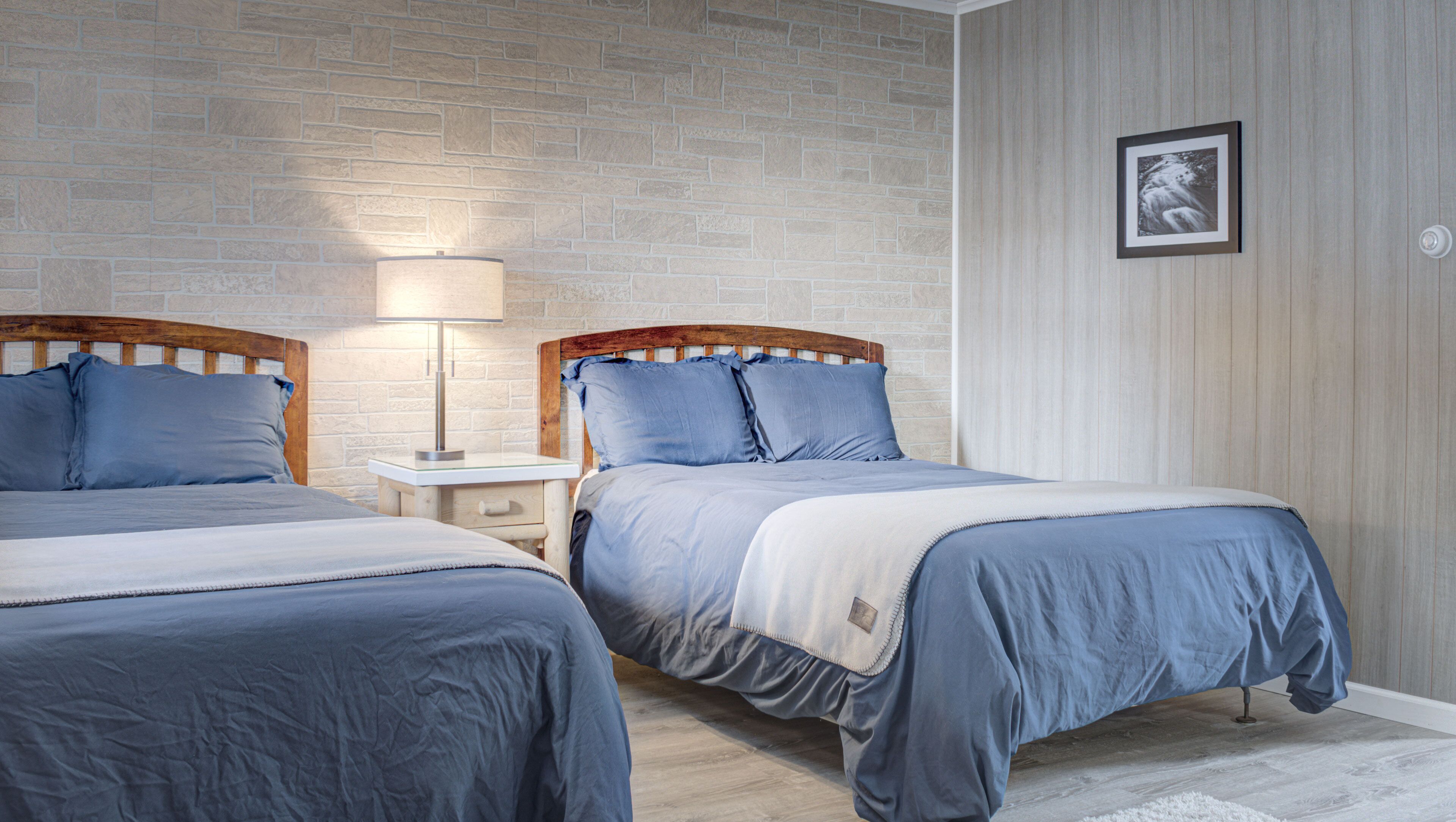 A bedroom with two beds, a nightstand, a lamp, and a framed picture on the wall.