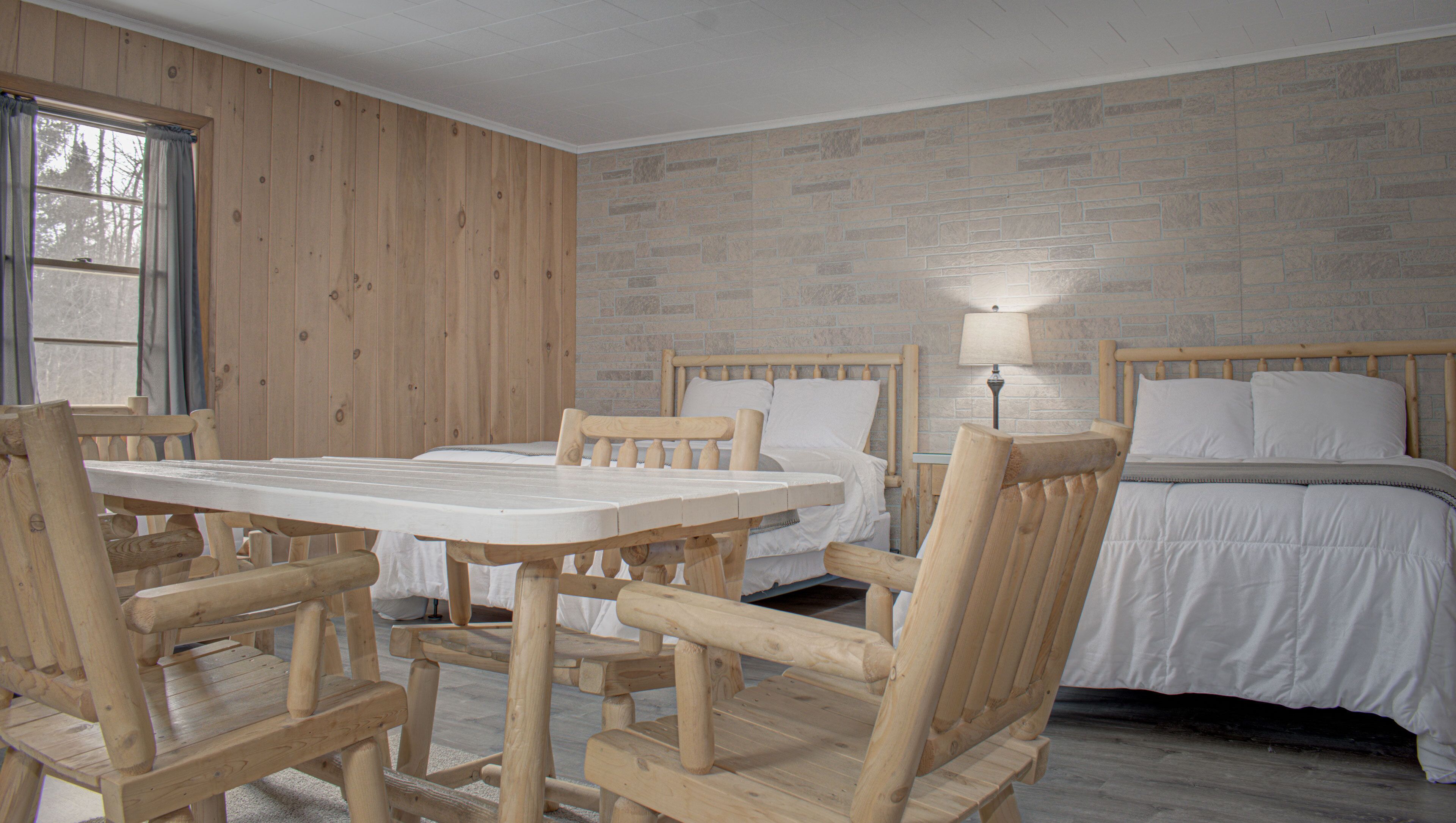 A room with a wooden table and chairs, two beds, and a window with curtains.