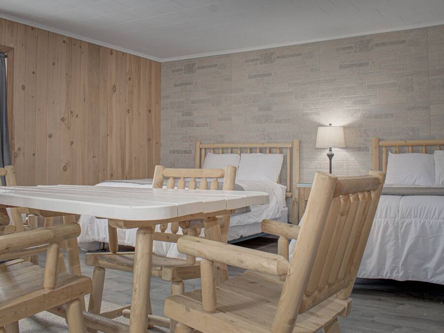 Una habitación con una mesa de madera y sillas, dos camas y una ventana con cortinas.