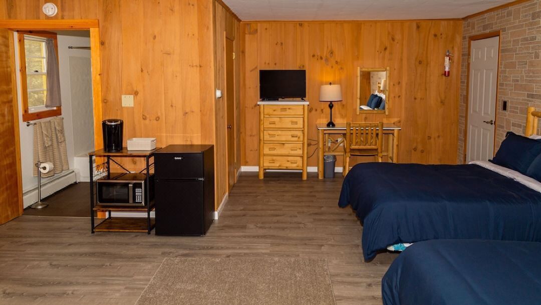 Una habitación con paredes de madera, una cama, un escritorio con una silla, un televisor y un microondas.