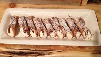 A white rectangular plate with a row of cream-filled pastries dusted with powdered sugar and drizzled with chocolate.