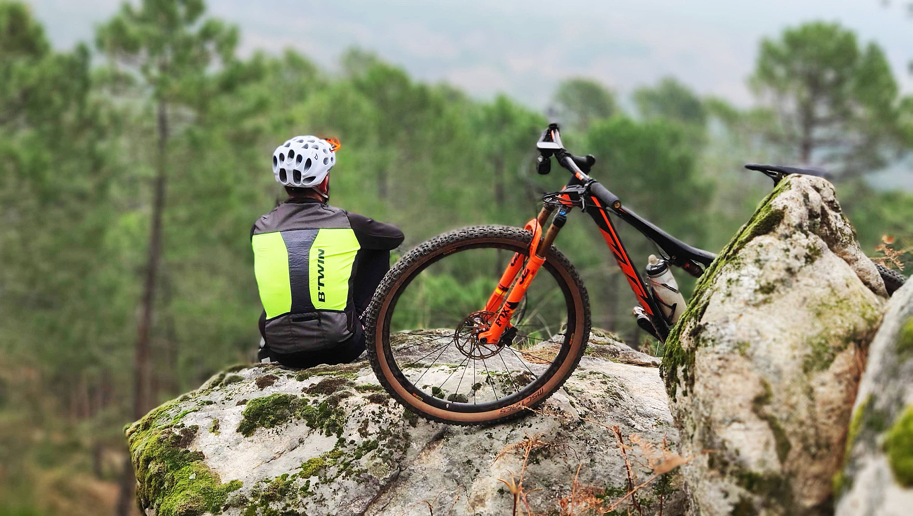 En person sidder på en mosbegroet sten med en mountainbike ved siden af.