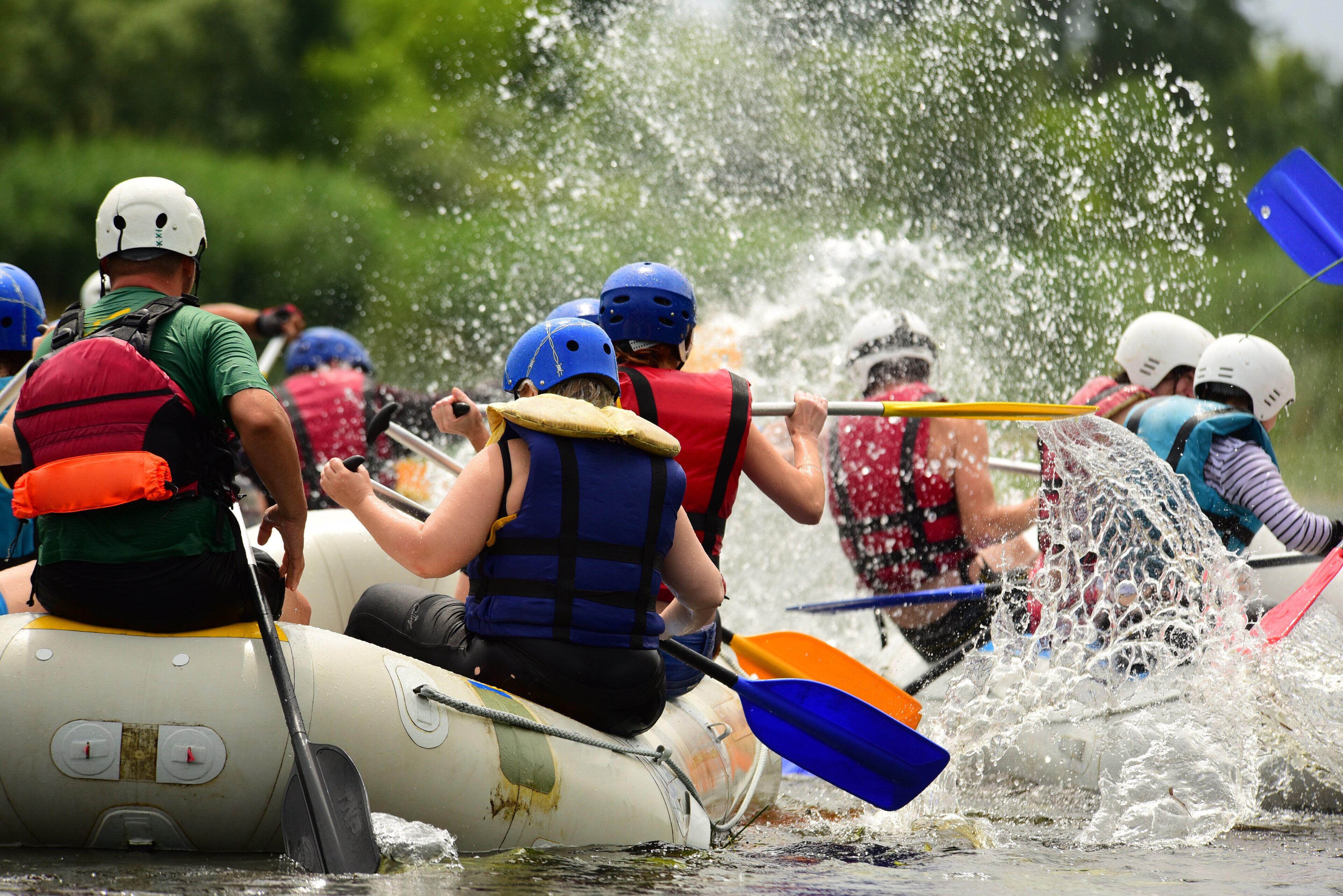 A group of people in a raft navigating through water, wearing life jackets and helmets.