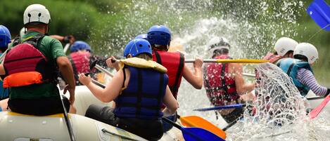 A group of people in a raft navigating through water, wearing life jackets and helmets.
