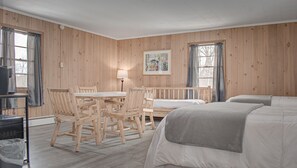 Huone, jonka seinät ovat puuta, ruokapöytä tuoleineen, sänky ja seinällä oleva taulu.