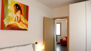 A hotel room with a bed, a nightstand, a painting, a red sofa, and a door leading to another room. - Venice Apartments Dante (Mestre)