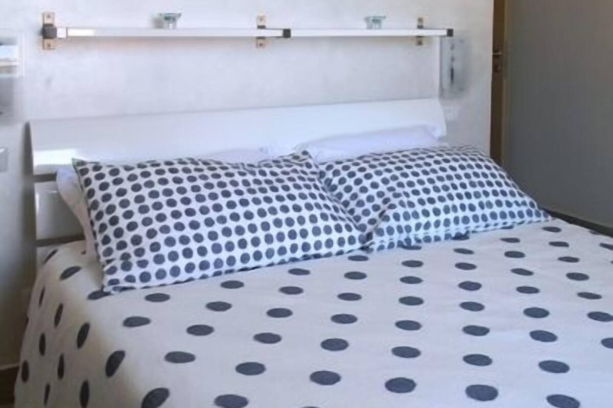 A bed with a polka dot bedspread, a white headboard, and a framed picture above the bed.