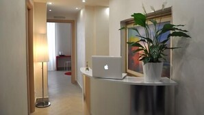 A hotel reception area with a laptop on a counter, a potted plant, and a painting on the wall. - Agli Horti Sallustiani bed & breakfast (Rome)