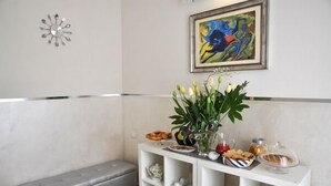 A modern living room with a white console table displaying a vase of flowers, a painting, and various food items. - Agli Horti Sallustiani bed & breakfast (Rome)