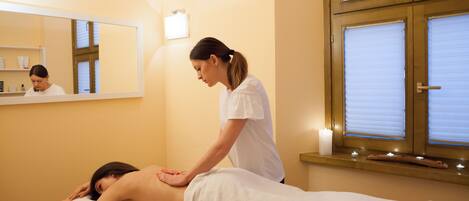 A massage therapy room with a massage table, a client lying face down, and a therapist standing beside.