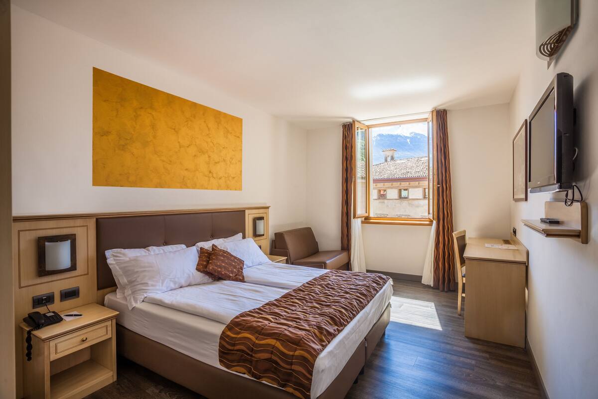 A hotel room with a bed, a desk, a chair, a TV, and a large window with curtains.