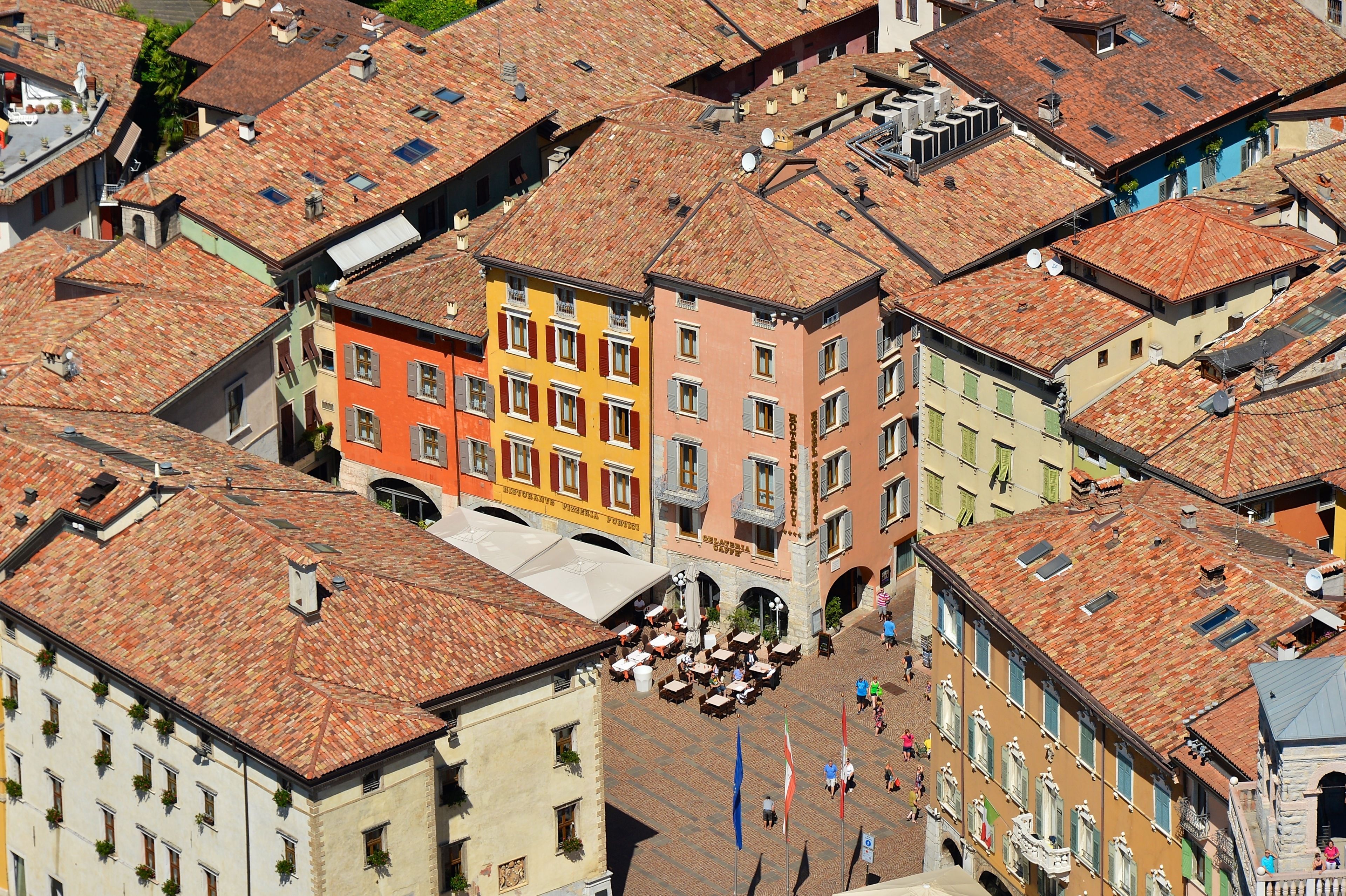 A historic square with colorful buildings, a central open area with tables and chairs, and flags.