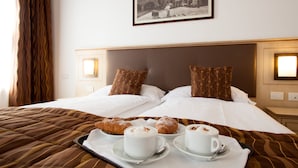 Habitación de hotel con una cama grande, dos almohadas, una bandeja con pasteles y café, y un cuadro en la pared.