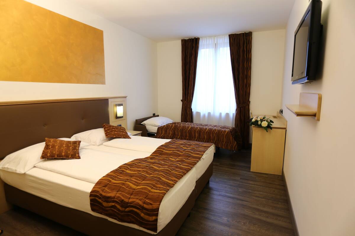A hotel room with two beds, a desk, a TV, and a window with curtains.