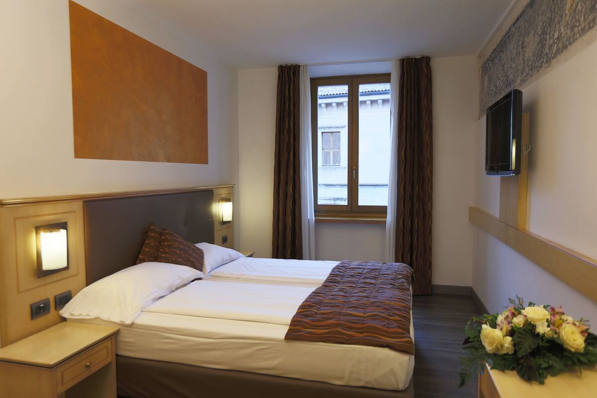 A hotel room with a bed, bedside table, lamp, and a window with curtains.
