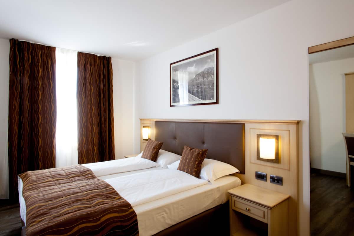 A hotel room with a double bed, two bedside tables, a nightstand, a framed picture on the wall, and a mirror.