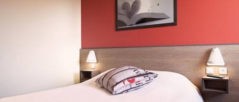 A neatly made bed with a heart-shaped pillow, a framed artwork on the wall, and bedside lamps.