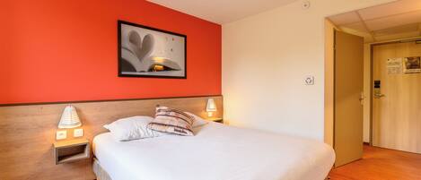 Una habitación de hotel con una cama, dos lámparas de noche, una mesita de noche, un cuadro en la pared y una puerta que da a otra habitación.