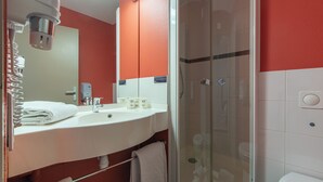 A bathroom with a white sink, mirror, and glass-enclosed shower. - ACE Hôtel Châteauroux Déols (Deols)