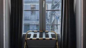 A view through a window with curtains, revealing a building with a tower and multiple rooftops. - Hotel Langlois (Paris)