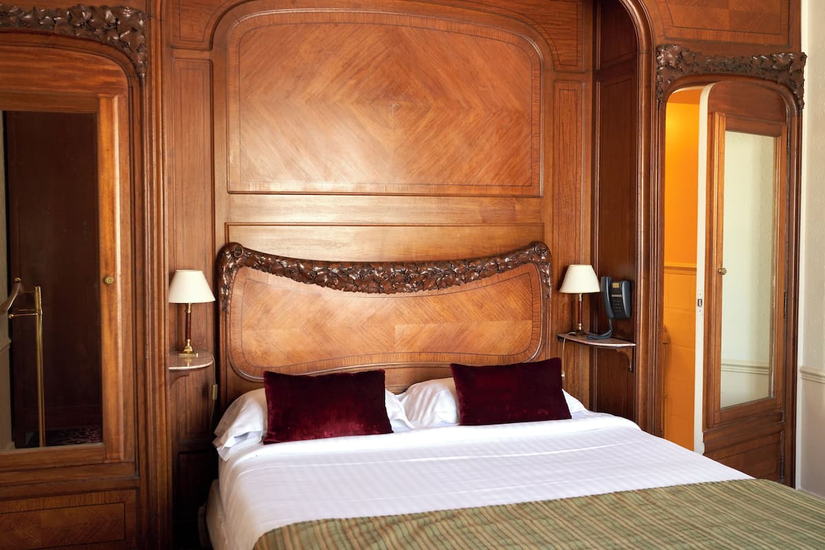 A large bed with a wooden headboard, two bedside lamps, and two red pillows.