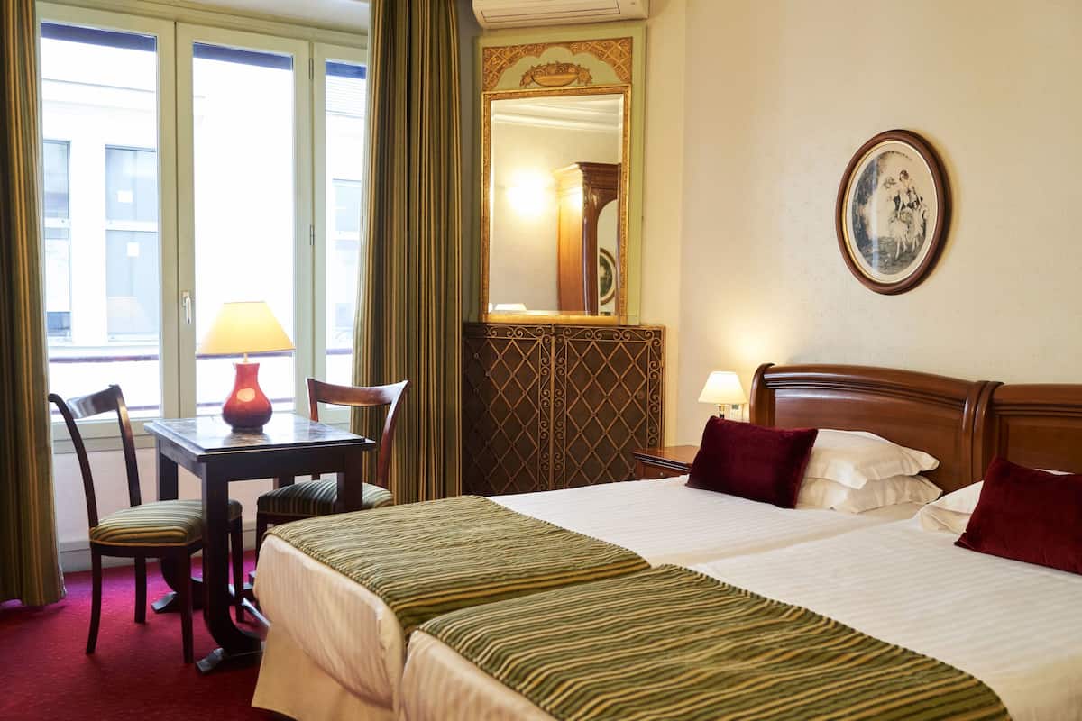 A hotel room with two beds, a desk with a lamp, a chair, and a large mirror.
