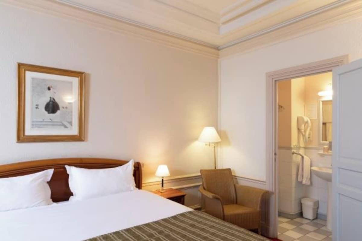 A hotel room with a bed, a chair, a lamp, and a framed picture on the wall.