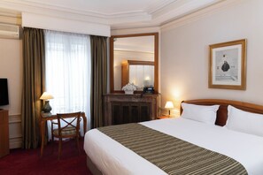 A hotel room with a large bed, a wooden desk with a lamp, a chair, a fireplace, and a framed picture on the wall. - Hotel Langlois (Paris)