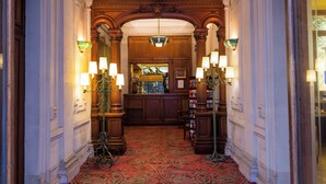 A grand hallway with ornate woodwork, a red patterned carpet, and multiple wall-mounted lamps. - Hotel Langlois (Paris)