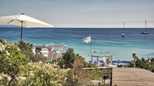 A coastal view with a wooden deck, white lounge chairs, and umbrellas overlooking the sea. - Smart Suite & Apartments (Santa Teresa di Gallura)