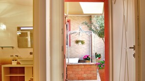 A hallway leading to a bathroom with a sink, a mirror, and a shower. There is a small seating area with a bench and a potted plant. - Smart Suite & Apartments (Santa Teresa di Gallura)
