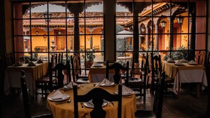 Un restaurante con mesas dispuestas para comer, vista a un patio con arquitectura tradicional y un ambiente cálido.